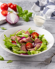 Salad with roast beef, tomato, onion, lettuce and mustard sauce on light background. Delicious healthy lunch with meat, diet food