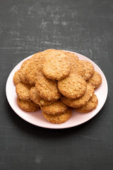 Cereal cookies on a pink plate on a black background, side view. Close-up.