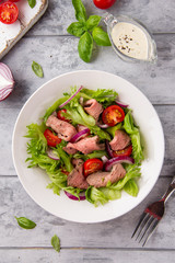 Salad with roast beef, tomato, onion, lettuce and mustard sauce on light background. Delicious healthy lunch with meat, diet food