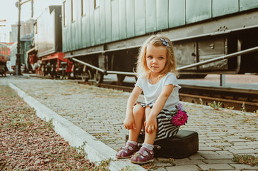A girl sits on a suitcase on the platform at the station near the train with flowers. I arrived home after a vacation at sea. Meeting, long trip
