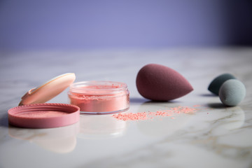 Looses Rouge Puder Make-up mit Blender Schwamm auf Marmor Beauty Schminktisch