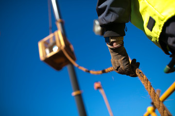 Rope access rigger worker commencing high risk job wearing heavy duty glove holding a safety tag line rope to control load swing while crane is lifting in construction building site, Perth Australia  - Powered by Adobe