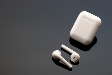 Wireless white headphones and case on black background, copy space, top view