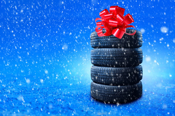 New winter tires pile as a gift. Tyres pile with a big red bow, as a present or bonus for buying a car. Banner with copy space. © Dmytro