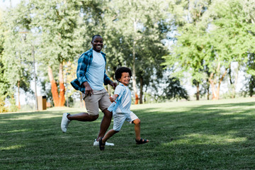 Obraz premium happy african american father and son running on grass