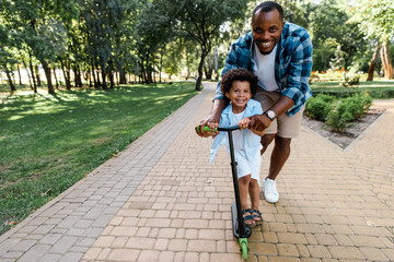 smiling african american father near cute son riding scooter © LIGHTFIELD STUDIOS