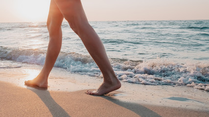 Legs of a young slender girl in black short dress walk along promenade of the sandy sea shore