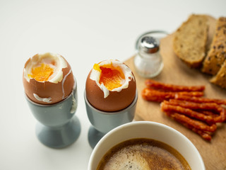 Pyszne, zdrowe śniadanie. Jajka na miękko z pieczywem, dodatkami i kawą leżące na białym tle. Widok z góry. - obrazy, fototapety, plakaty