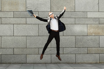 Young and cheerful businessman in suit jump on urban background. Success and victory, positive lifestyle. Award, reward.