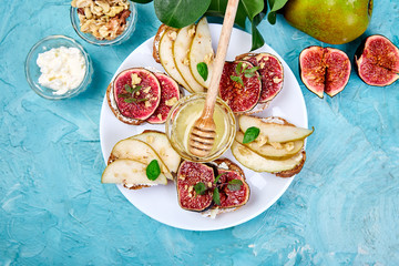 Fototapeta na wymiar Bruschetta and Crostini with pear, ricotta cheese, honey, figs, nuts and herbs. Breakfast toasts or snack sandwiches. Antipasto. Italian food. Top view. Copy space.