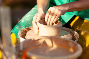 Hand craft making pottery on wheel. Female hands mold ceramic plate from clay (pot).