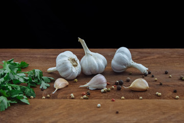 Heads and cloves of garlic lying on a brown wooden kitchen table with a bunch of green parsley and...