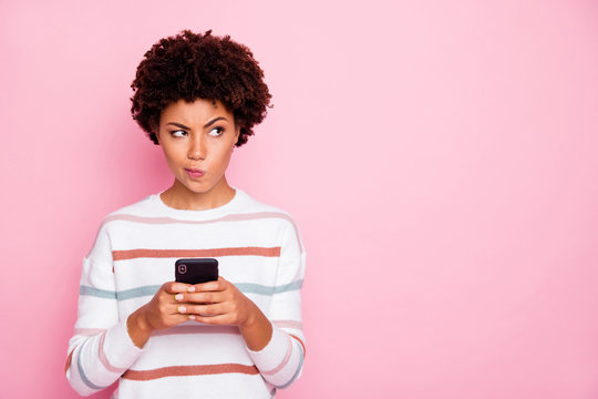 Photo Of Pretty Dark Skin Lady Holding Telephone Doubtful About New Instagram Post Wear White Striped Pullover Isolated Pastel Pink Color Background