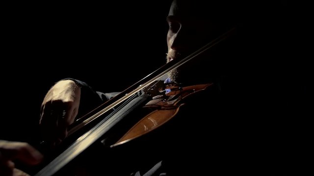 A man plays the violin in a dark room. Black background. Close up