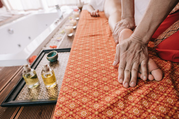 cropped view of masseur doing foot massage to woman in spa salon