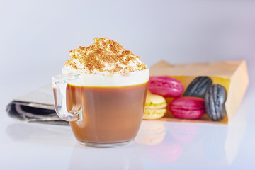 Coffee, cappuccino in a glass mug with whipped cream and ground nut. Macaron cakes in a paper bag, newspaper. The photo.