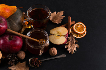 Tea, may liquid honey, apples, fruits, cinnamon, dried oranges and nuts on a black background. autumn harvest, copy space.