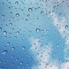 Water drops on glass with blue sky and clouds background. Abstract texture.