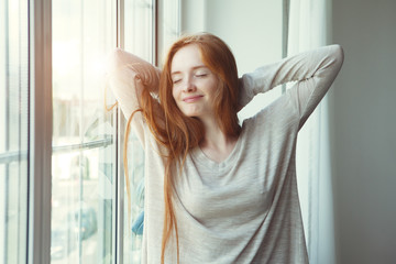happy young red hair woman waking up, stretching, raising hands, morning sunshine, happy new day, day off