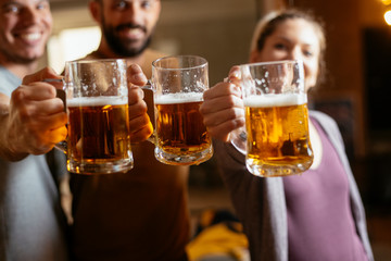 Group of happy friends drinking and toasting beer at bar 