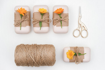 Handmade natural soap set decorated with craft paper, orange calendula flowers, skein of twine and scissors on white background . Organic cosmetics concept. Top view Flat lay Template for design