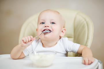 smiling baby in a feeding chair holds a spoon in his mouth and smiles