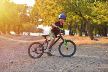 Fototapeta premium Happy kid boy of 7 years having fun in autumn park with a bicycle on beautiful fall day. Active child wearing bike helmet