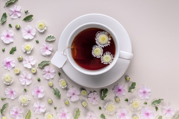 Obraz na płótnie Canvas Flavored herbal tea in a white ceramic cup with a saucer. Floral pattern on a beige background. Flower tea concept. Tea bag. Copy space