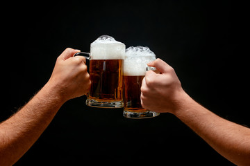 Hands toasting with beer on black background