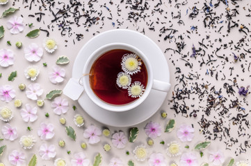 Flavored herbal tea in a white ceramic cup with a saucer. Floral pattern on a beige background. Flower tea concept. Tea bag. Top view
