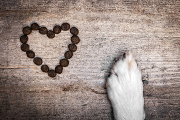 Dog´s Paw and heart shaped goodies or kibbles on wooden Table, copyspace