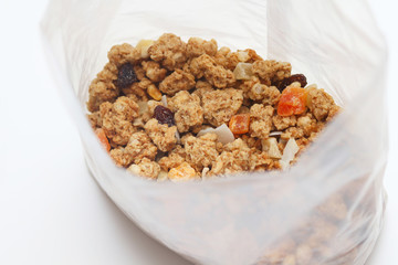 Granola with fruits and nuts in a transparent plastic bag. Baked muesli mix. Super food concept. Breakfast cereals. Kids diet. White isolation background.