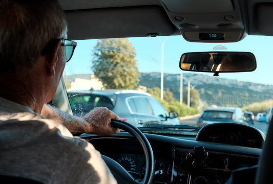 old senior man 60s 70s driving in his car on the traffic in the center of the city in a sunny day.