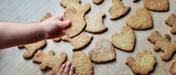 christmas gingerbread cookies in various form on the wooden background. Little hand of child holding a heart cookie.  Panoramic banner.