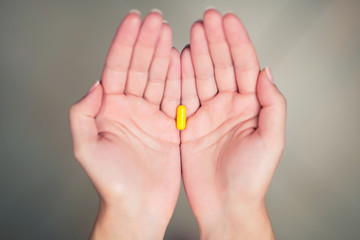 Yellow pill lies in female palms folded together, top view