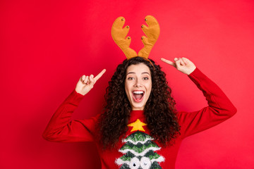 Portrait of shocked crazy cheerful student girl point index finger her yellow reindeer headband enjoy x-mas masquerade party wear stylish sweater with christmas tree ornament isolated red color