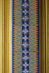 Detail from decorative patterned ceramic tiles bordered by gold wooden frames as part of the architecture on the wall of an ancient Buddhist temple in south east Asia