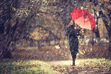 October walk in the rain, a young woman with a red umbrella in the autumn city park, autumn look - Powered by Adobe