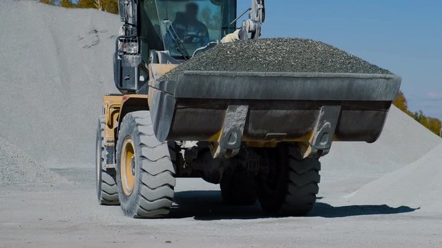 yellow bulldozer carries gray gravel on the background of heaps of stone.