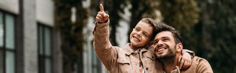 panoramic shot of smiling son and dad embracing in autumn day on street