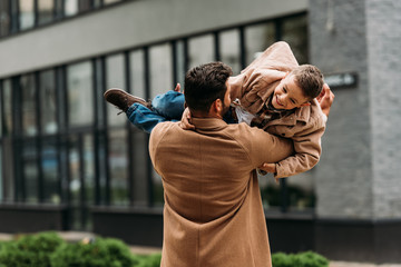 back view of father in coat holding smiling son on street