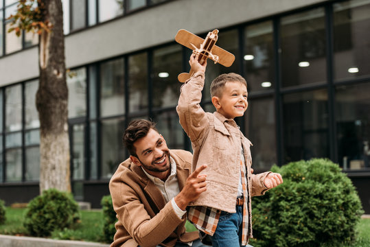father in stylish coat and smiling son holding toy plane on street
