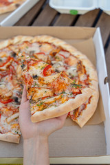 Woman is eating hot chicken pizza with mushrooms and bell pepper with a thick crust on a summer terrace