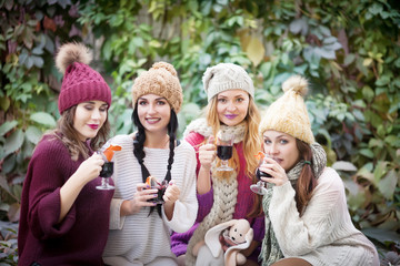 Young women drink mulled wine in autumn park. Sunny autumn day. Outdoors lifestyle fashion portrait. Positive emotions.