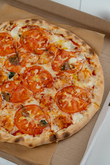 Pizza Margherita with cheese and tomatoes in a cardboard box close up