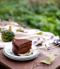 beautiful outdoor still life in autumn garden with tasty slice of chocolate cake on vintage plates stands on rustic wooden table with grey napkin and pumpkins, selective focus