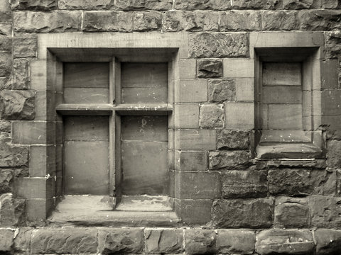 monochrome sepia image of ancient blocked up stone window frames in a rough weathered wall