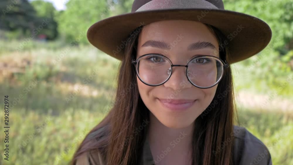 Poster close up view of cheerful cute young brunette woman in brown hat smiling and fixing her hair with ha