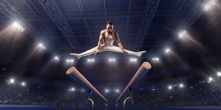 Male athlete doing a complicated exciting trick on parallel bars in a professional gym. Man perform stunt in bright sports clothes