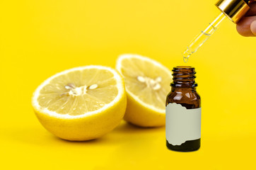 Little bottle of lemon essential aroma oil with pipette and drops in hand on yellow background